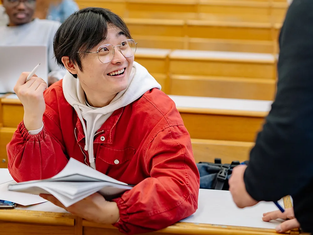 A student in a lecture hall looking up mid-conversation with a member of faculty