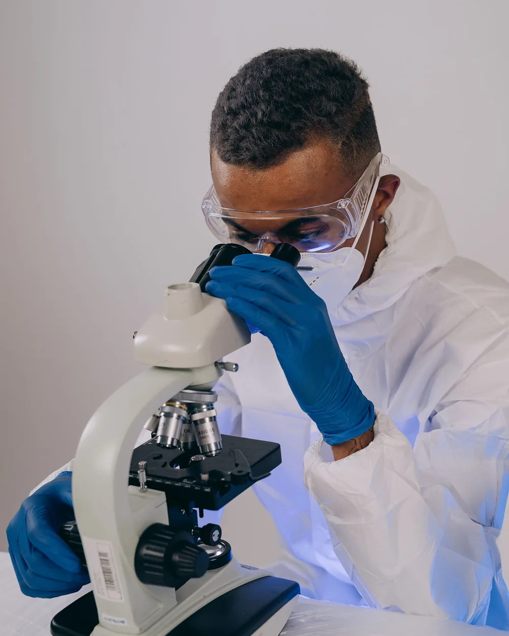 A researcher in safety glasses and gloves looking through a microscope