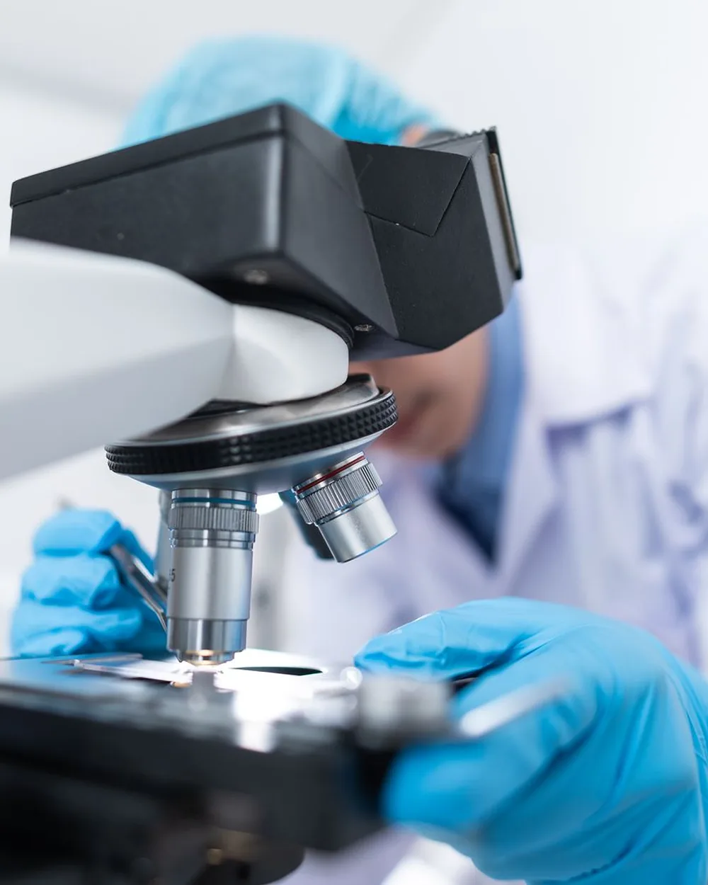 A scientist adjusting a sample on a microscope stage with gloved hands