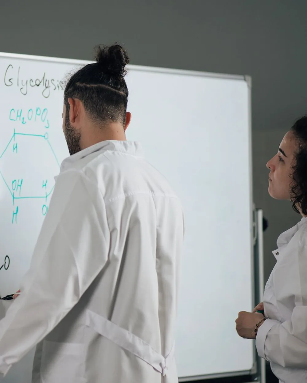 Two scientists in lab coats working through formulas on a whiteboard